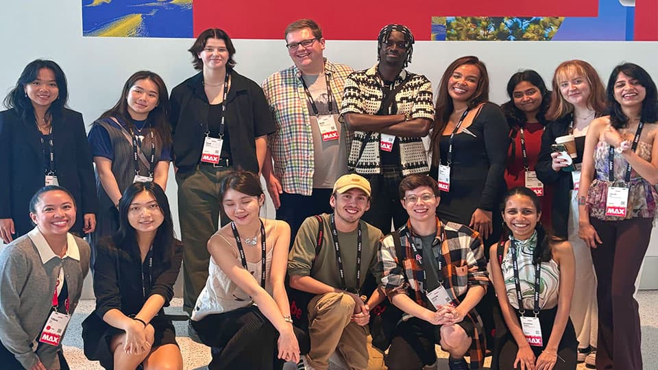 A group of 15 standing in front of a red sign with text in white letters, MAX, at The Digital Edge Awards winners, Adobe Max 2024.
